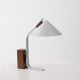 Minimalist desk lamp seen three quarters on against a pale ground