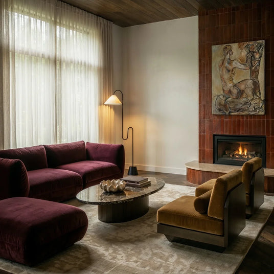 The lamp lit near a fireplace with a burgundy sofa, an armchair and a rug