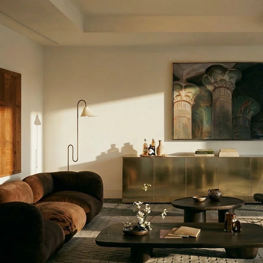 The lamp lit in a living room beside a metal sideboard, artwork and a low table
