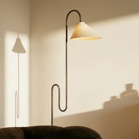 The cone shade lit, its own shadow thrown across the wall behind the stem