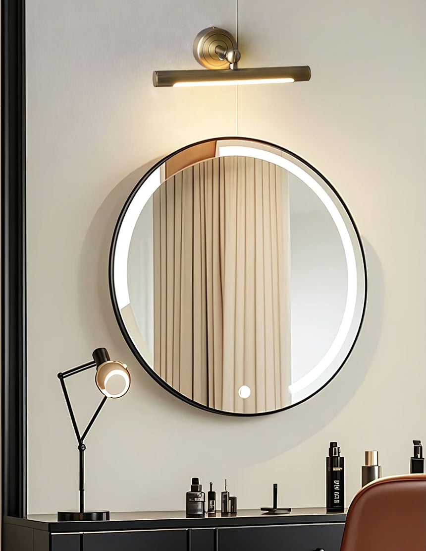Bronze bar lit above a round black framed mirror over a dark vanity with a chair