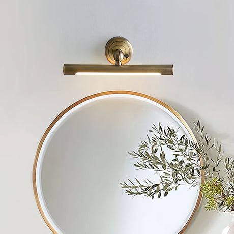 Bronze bar lit above a round gold mirror with olive branches on a pale wall