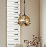 The amber mirrored globe lit in front of a venetian blind and a plant