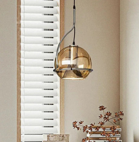 The amber mirrored globe lit in front of a venetian blind and a plant