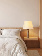 Ribbed shade lamp lit on a nightstand beside a bed with white linen