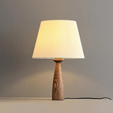 Ribbed shade lamp lit warm against a pale wall with its cord trailing