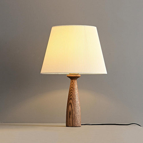 Ribbed shade lamp lit warm against a pale wall with its cord trailing