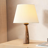 Ribbed shade lamp lit on a pale wood cabinet beside a closed book