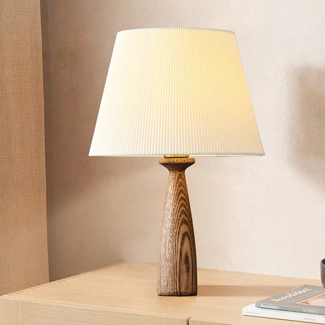 Ribbed shade lamp lit on a pale wood cabinet beside a closed book