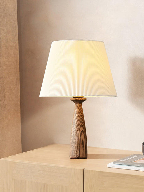 Ribbed shade lamp lit on a pale sideboard beside a closed notebook