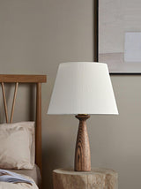 Ribbed shade lamp unlit on a wood stump table beside a made bed
