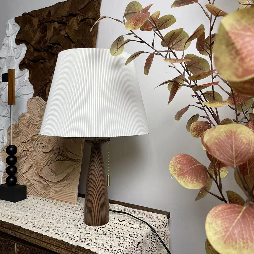Ribbed shade lamp unlit beside dried branches and a carved panel