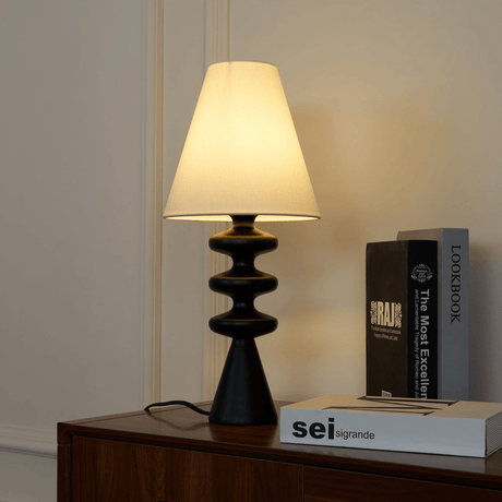 Rippled base lamp lit on a walnut sideboard beside a book