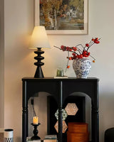 Rippled base lamp lit on a console beside a blue and white vase