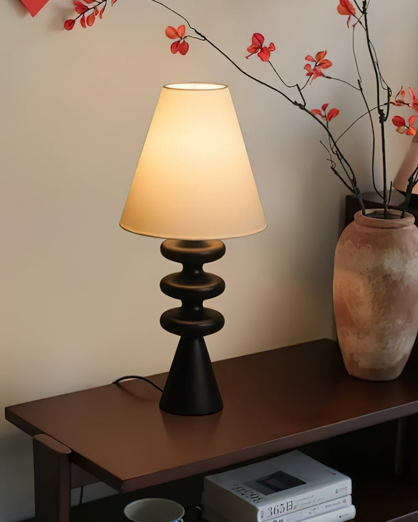 Rippled base lamp lit on a console beside branches in a stone vase