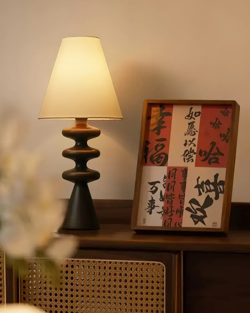 Rippled base lamp lit beside a framed scroll and a cane chair