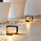 Two low bodies lit in a white pebble bed beside a pale terrace