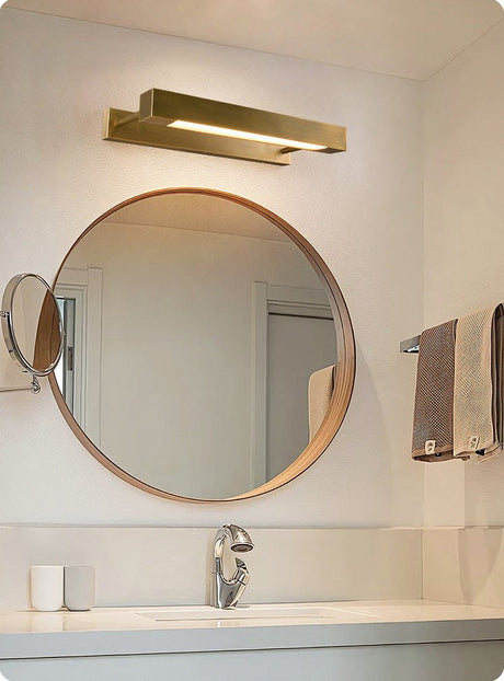 Brass bar above a round mirror over a basin with a folded towel nearby