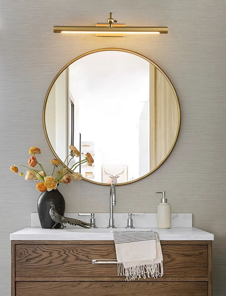 Gold bar lit above a round mirror over a walnut vanity with a basin and a towel