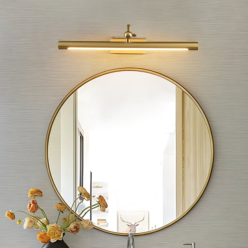 Gold bar lit above a round gold mirror beside dried orange flowers in a vase