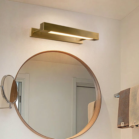 Brass bar lit above a round mirror in a bathroom with a hanging towel