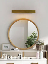 Brass bar above a round mirror over a white vanity with plants and frames