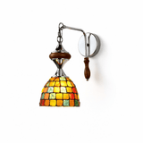 The amber and green mosaic shade on its chrome arm, walnut grip below