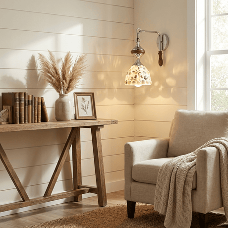 The sconce with a patterned shade above a wood console and a cream armchair