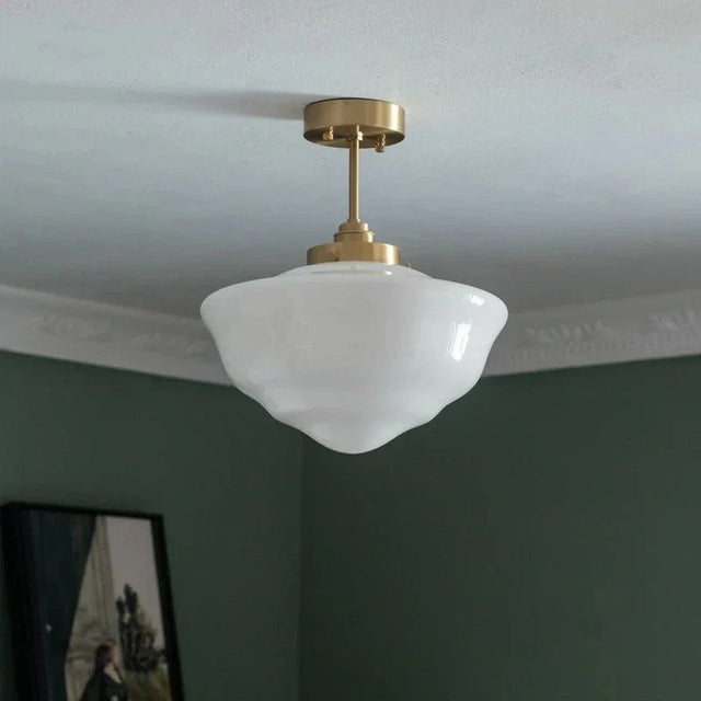 A single opal schoolhouse shade on a brass fitting against a dark green wall