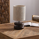 Black pebble nightstand table lamp on a wooden table beside an open book