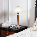 Nightstand table lamp lit on a dark nightstand beside a made bed