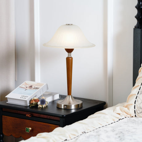 Nightstand table lamp lit on a dark nightstand beside a made bed