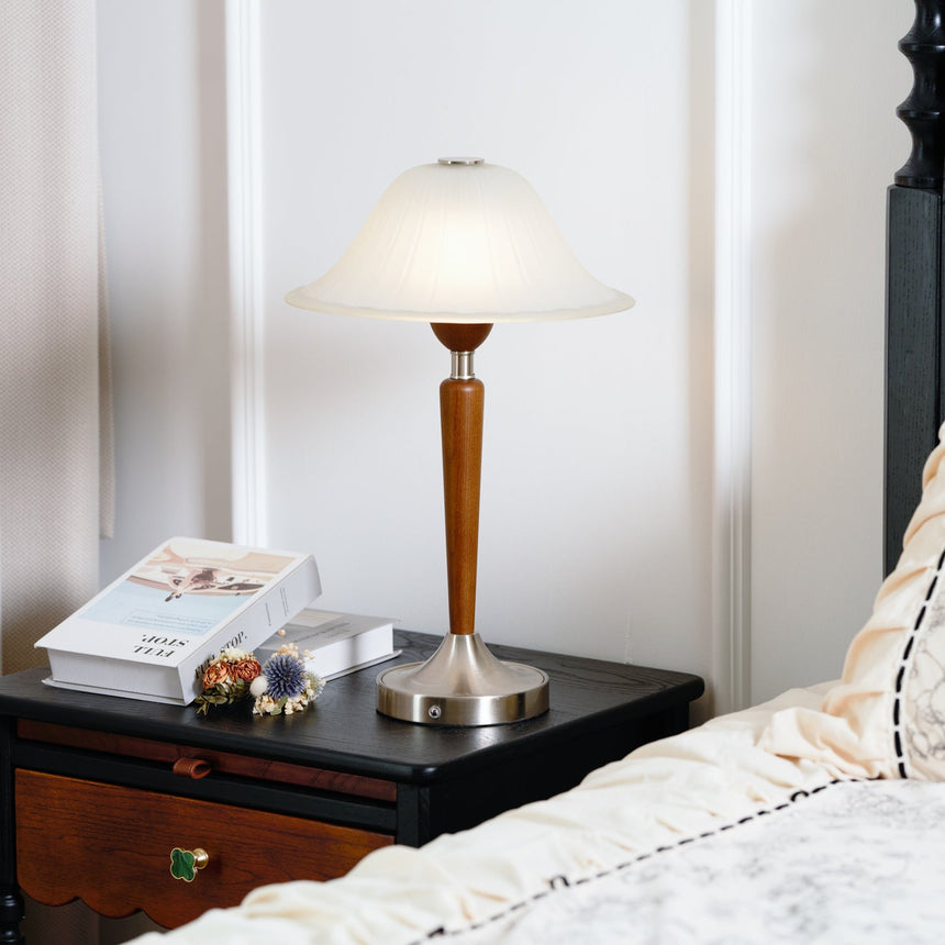Nightstand table lamp lit on a dark nightstand beside a made bed