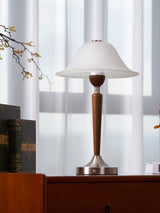 Nightstand table lamp lit on a cherry chest beside a sheer curtain