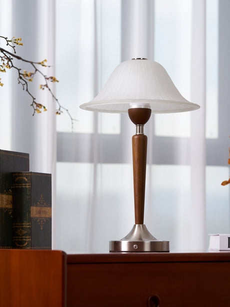 Nightstand table lamp lit on a cherry chest beside a sheer curtain