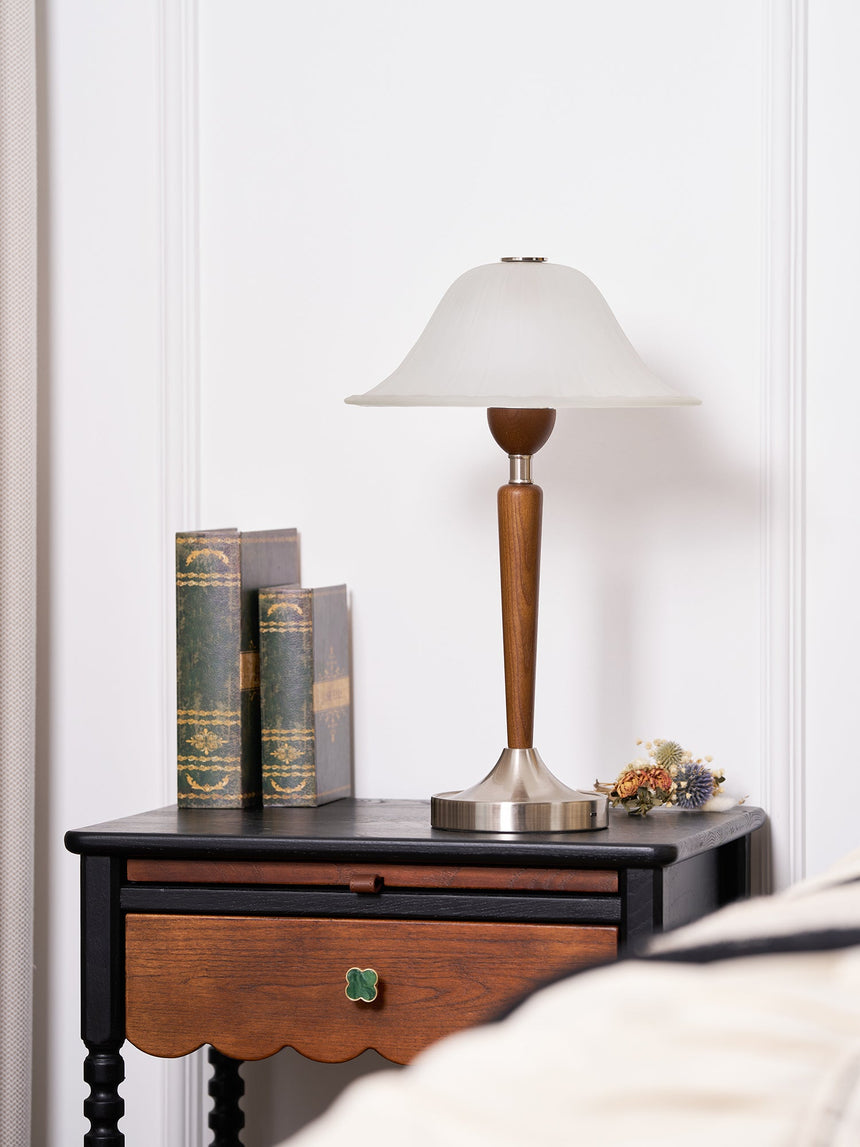 Nightstand table lamp lit on a nightstand beside a dark spindle headboard