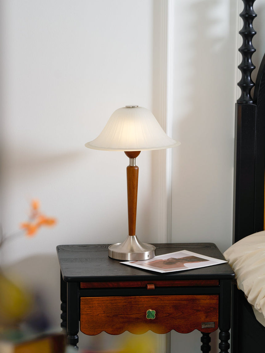 Nightstand table lamp lit on a nightstand beside a turned dark bedpost