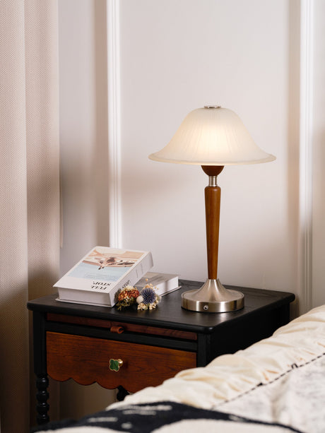 Nightstand table lamp lit on a nightstand in front of a sheer curtain