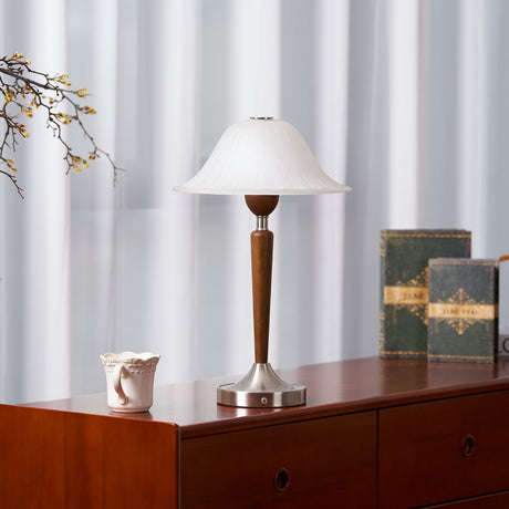 Nightstand table lamp lit on a cherry chest of drawers beside books