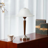 Nightstand table lamp lit on a cherry chest beside a small white jug