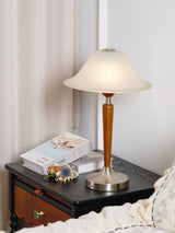 Nightstand table lamp lit on a nightstand beside a small brooch and books