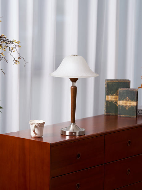 Nightstand table lamp lit on a cherry chest with a jug and old books
