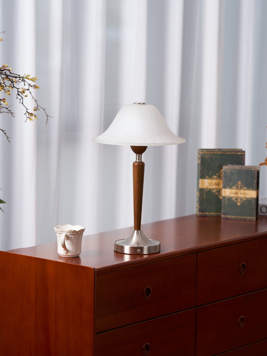 Nightstand table lamp lit on a cherry chest with a jug and old books