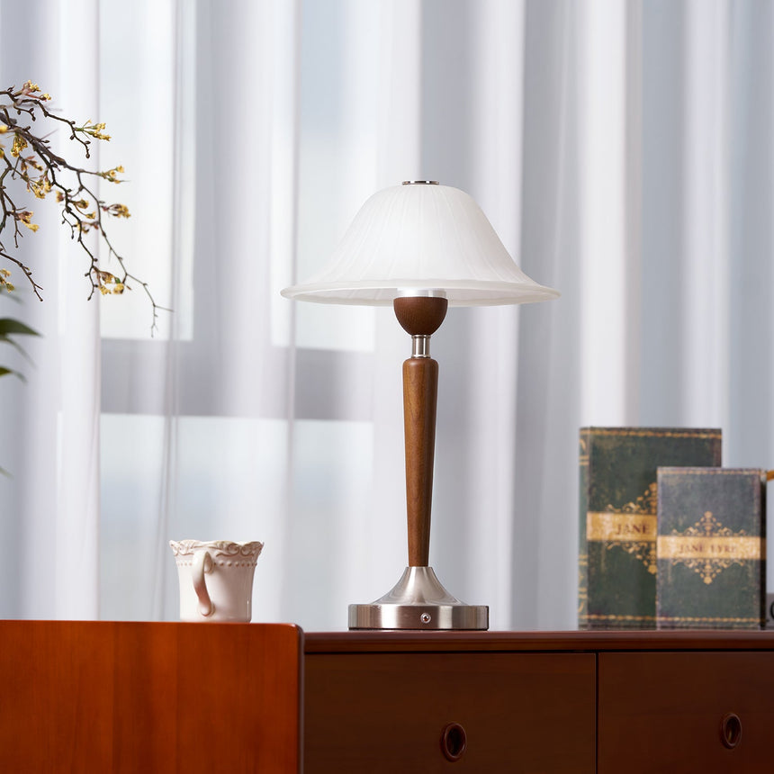 Nightstand table lamp lit on a chest beside a small dark vase