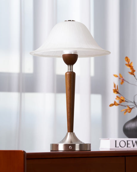Nightstand table lamp lit on a chest beside a sprig of orange blossom