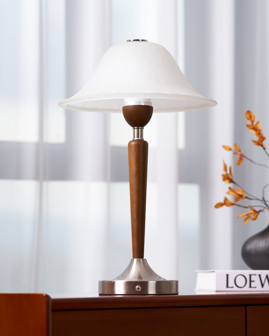 Nightstand table lamp lit on a chest beside a sprig of orange blossom