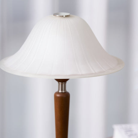 Close view of the frosted glass bell shade lit above the walnut stem