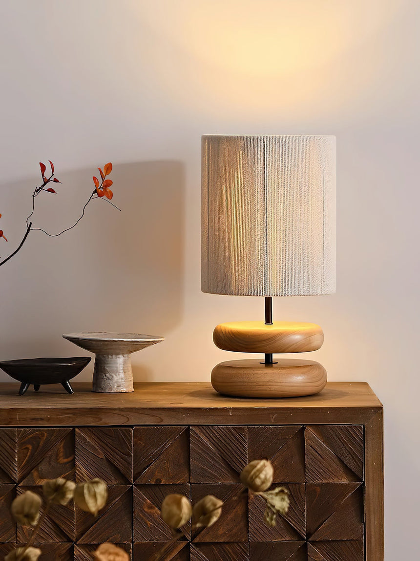Wood pebble nightstand table lamp lit beside a pale vase