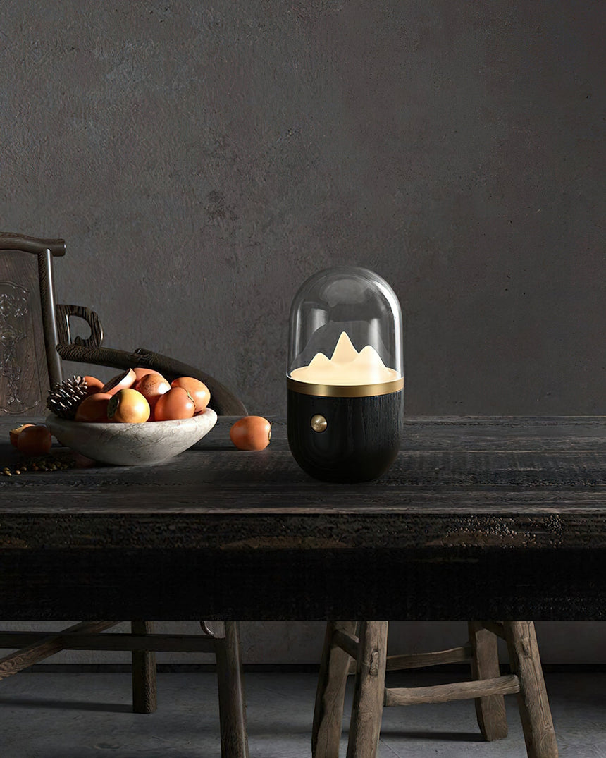 Black based nursery table lamp lit on a dark table beside a bowl