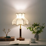 White blossom shade lamp lit warm, the scalloped hem in silhouette